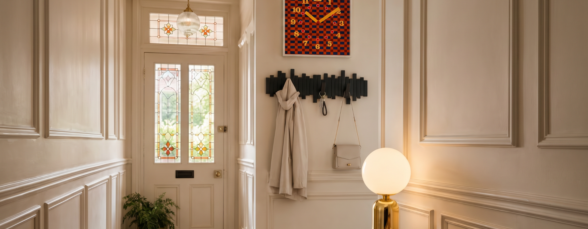 Stylish cream hallway with wall hooks, hanging coat and bag, warm globe lamp and decorative wall clock for practical entryway organisation.