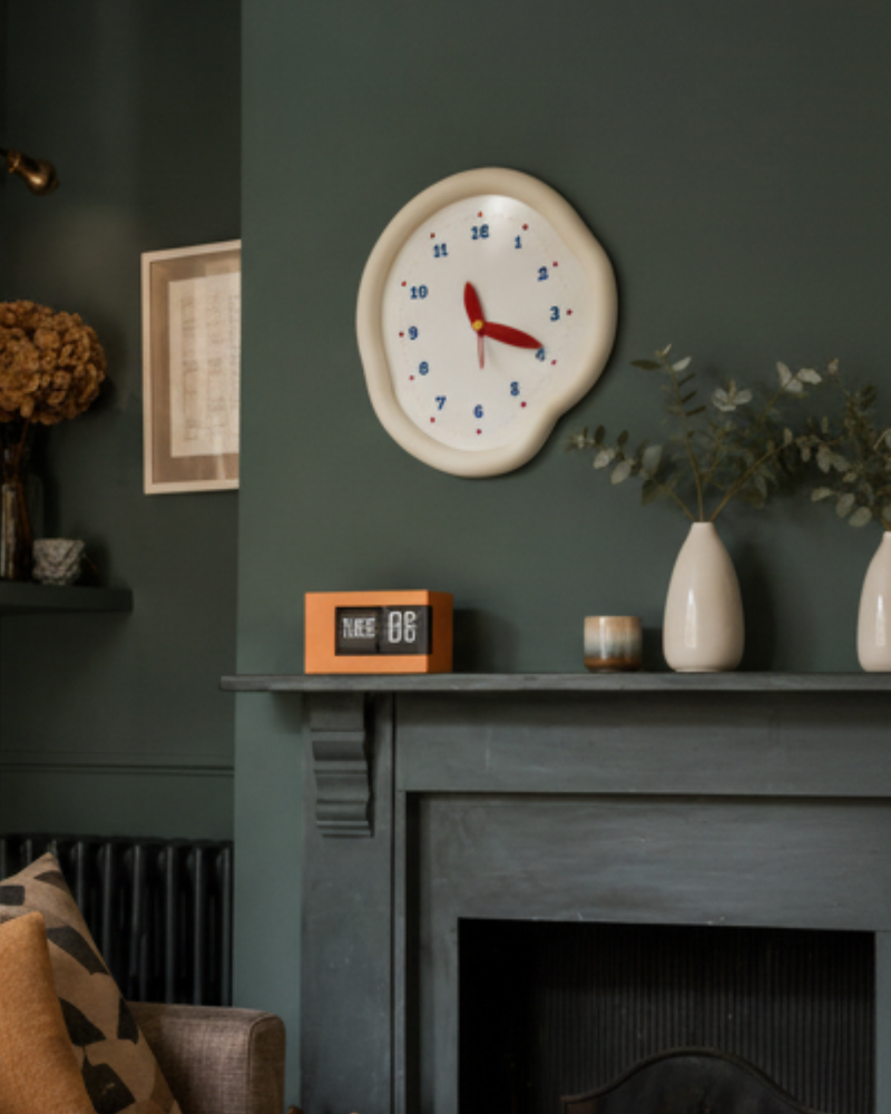 Cream irregular wall clock and orange flip clock styled on a dark green mantel, creating a cosy vintage-inspired living room look for UK homes.
