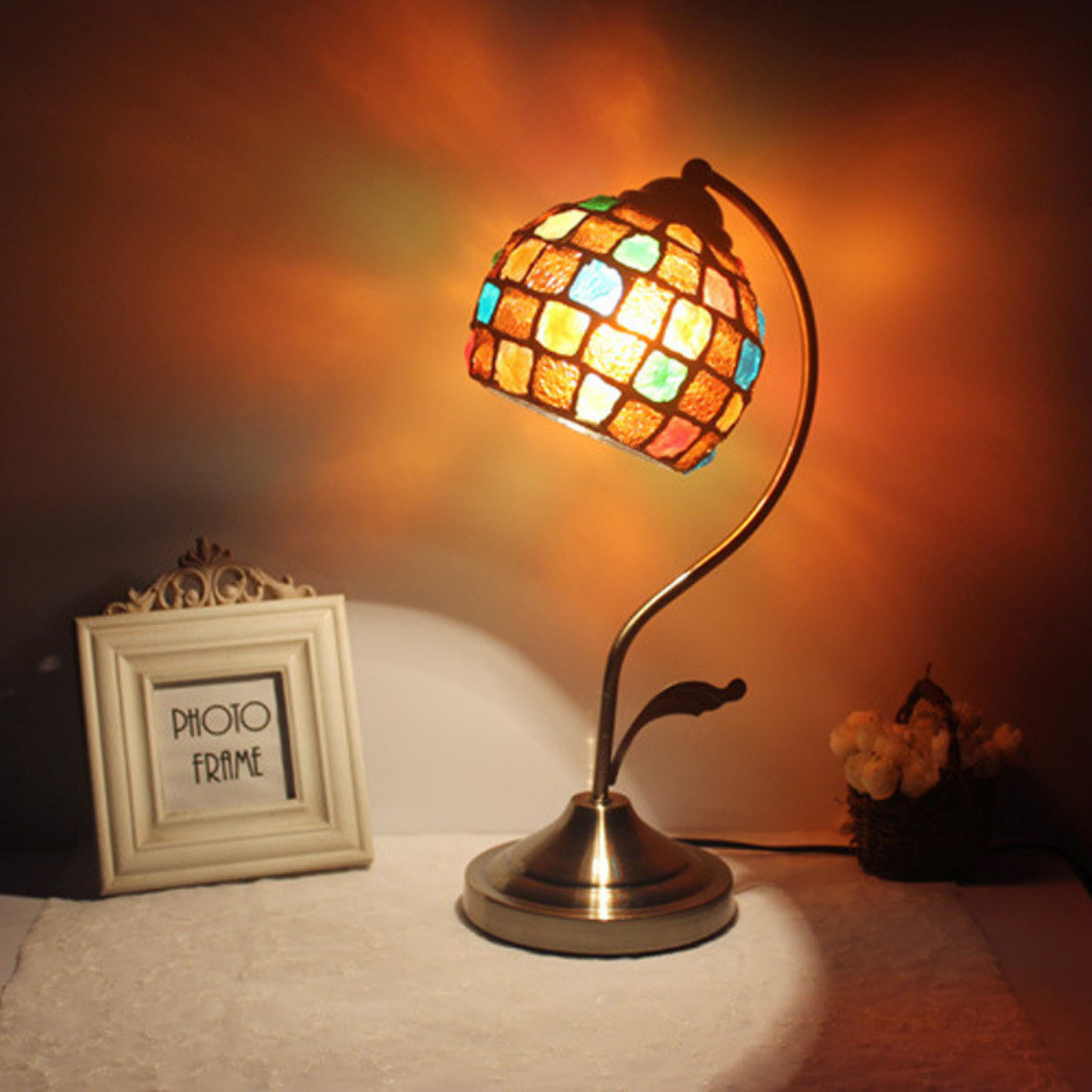 Vintage Tiffany-style stained glass table lamp with curved bronze stand and multicolour mosaic shade, casting a warm artistic glow for classic living rooms or bedside décor
