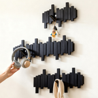 Black wall-mounted coat rack with geometric design holding various items on a white wall in the living room