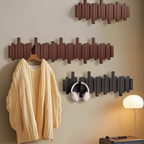 Wall-mounted coat rack with hooks holding a sweater and headphones against a neutral wall.