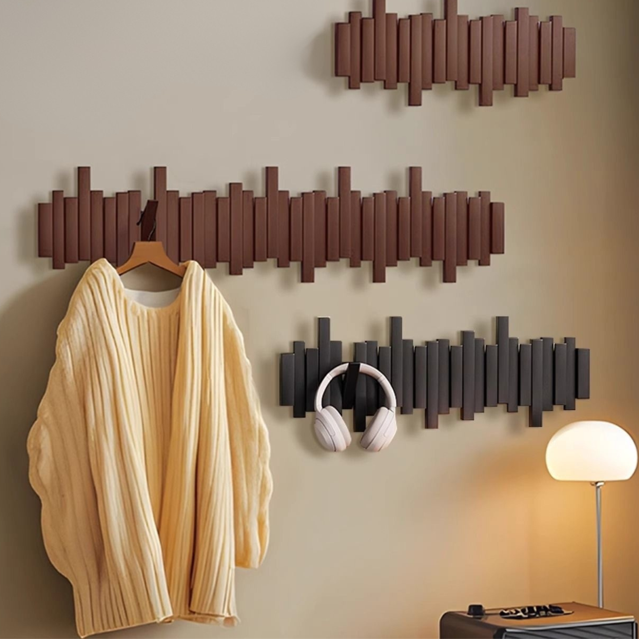 Wall-mounted coat rack with hooks holding a sweater and headphones against a neutral wall.