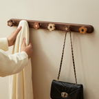 Wooden wall hook with floral designs holding a white garment and a black handbag against a beige wall.
