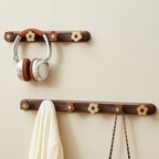 Wooden wall hooks with floral designs holding a pair of headphones and a towel on a beige wall.