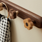 Wooden coat rack with decorative hooks on a neutral wall.