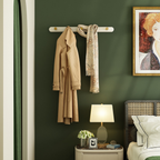 Coat and scarf hanging on a wall-mounted rack in a room with a lamp, plant, and framed picture.