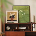 Sage Flight and Ochre Bloom framed wall art layered on a mid-century wooden console in a warm neutral living room.