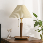 Arden Pleat Table Lamp with its light switched off, featuring a cream pleated shade and warm tapered base on a wooden side table.