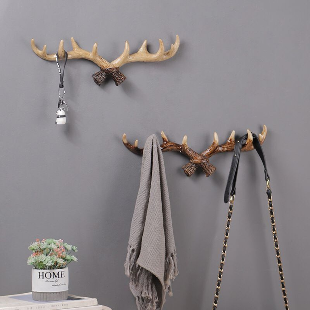 Two decorative wall hooks with antler design on a gray wall, with a plant and books below.