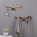 Two decorative wall hooks with antler design on a gray wall, with a plant and books below.