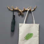 Decorative wall hook with antlers, green umbrella, and tote bag with leaf design on a gray background