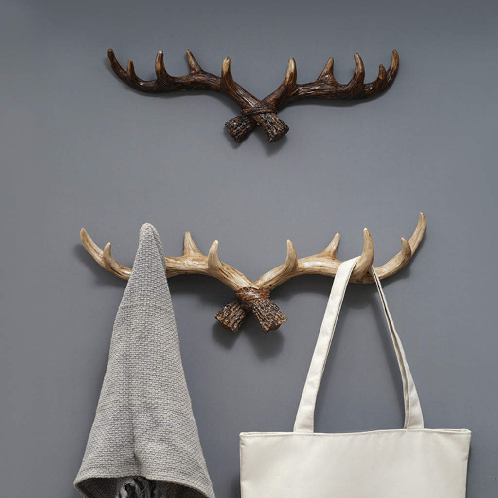 Two wall-mounted antler-shaped hooks with a gray towel and white bag hanging on them against a gray wall.