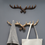 Two wall-mounted antler-shaped hooks with a gray towel and white bag hanging on them against a gray wall.