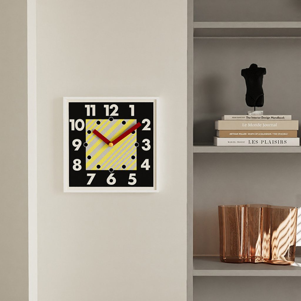 A bold square wall clock with oversized numbers, striped centre detail and red hands for kitchens, hallways and living rooms.