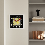A bold square wall clock with oversized numbers, striped centre detail and red hands for kitchens, hallways and living rooms.