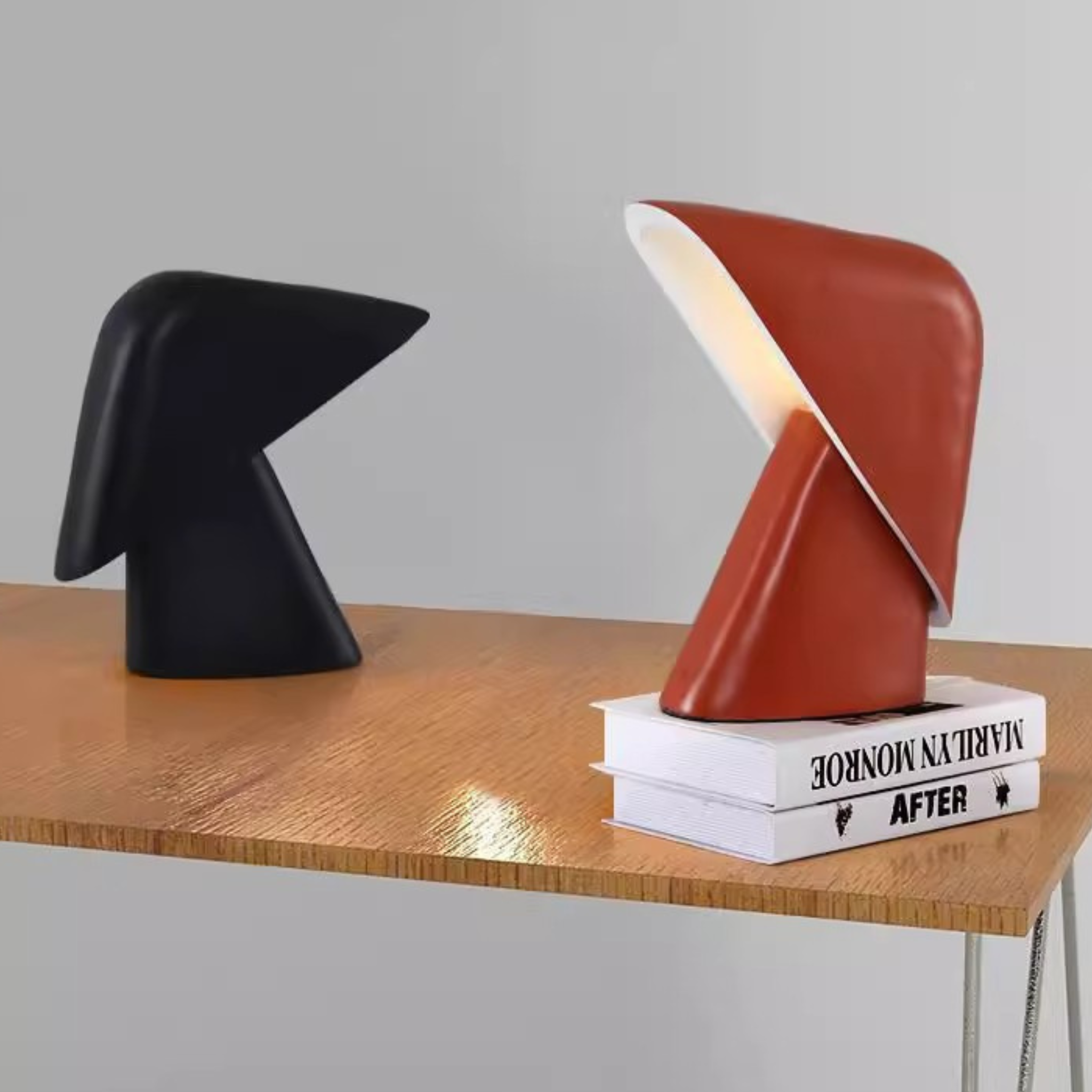 Black and orange modern table lamps on a wooden surface with books underneath.
