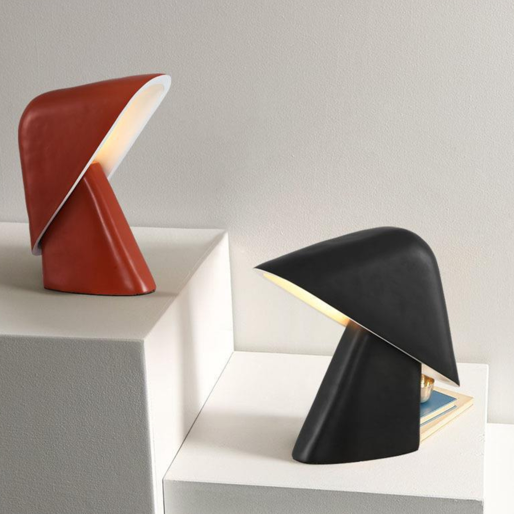 Two modern table lamps, one orange and one black, on a light gray surface.