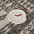 A soft ivory pebble-shaped wall clock with blue numbers and red hands, designed for UK bedrooms, kitchens, hallways and cosy living room walls.