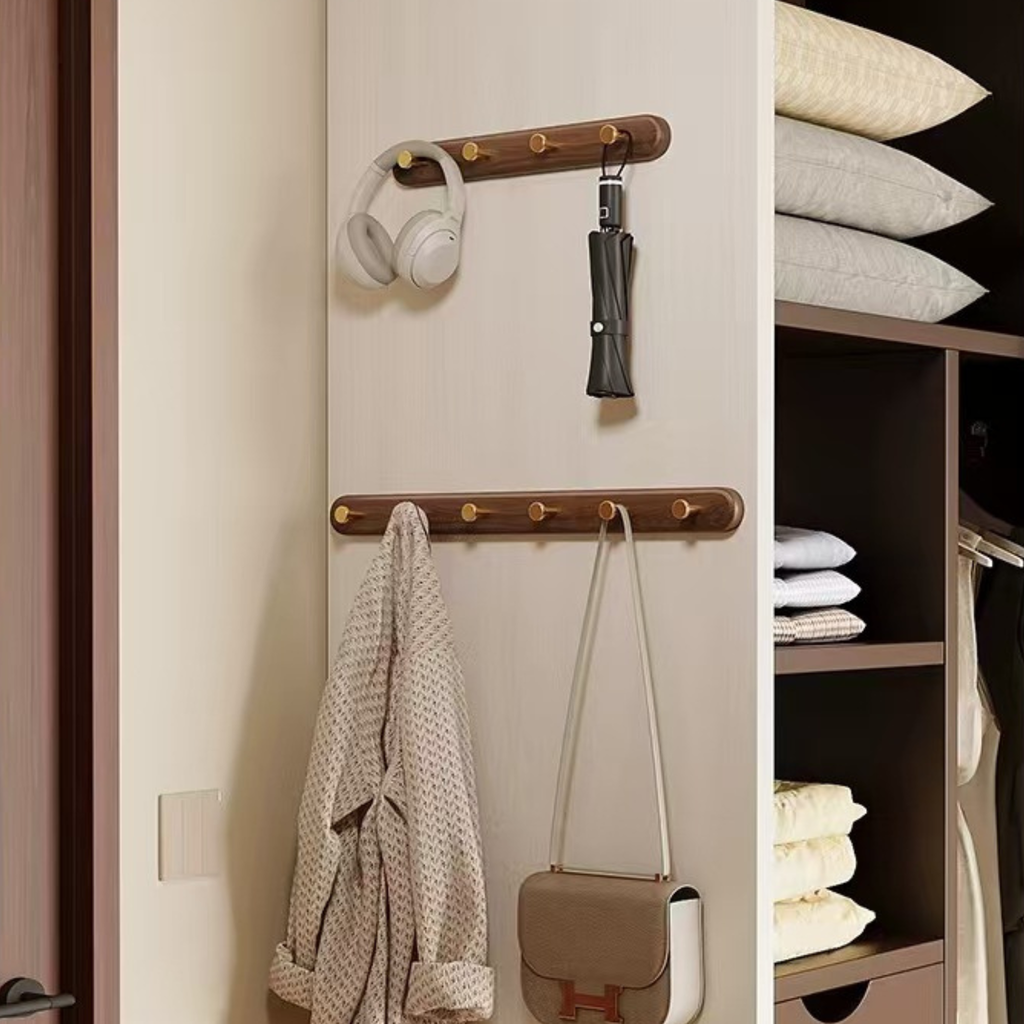 Wall-mounted coat rack with hooks holding a robe, handbag, and other items next to a closet with folded clothes.