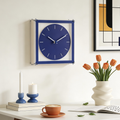 Blue wall clock on a white wall with decor items like a vase of tulips, candles, and a cup.