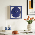 Blue wall clock on a white wall with decor items like a vase of tulips, candles, and a cup.