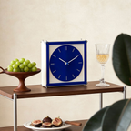 A blue square table clock with a bold round dial, perfect for shelves, desks, bedside tables and modern UK home styling.