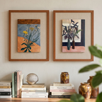 Still Bloom botanical framed wall art set styled above books with warm earthy tones, vases and wildflower artwork in a cosy living room.