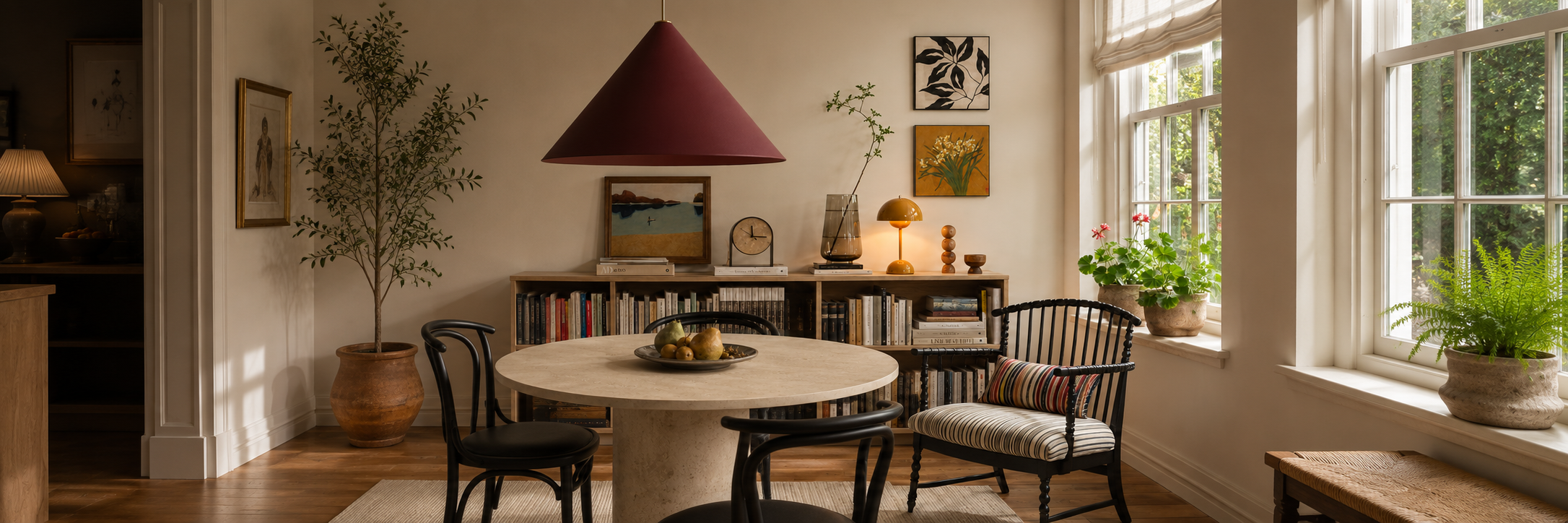Warm dining room featuring a statement pendant light, portable table lamp, bookshelves and natural daylight creating a cosy modern interior.